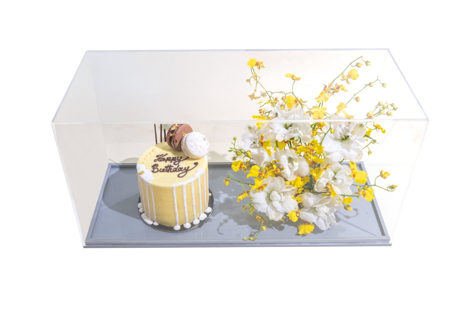 A decorative cookie cake with white and yellow flowers in a clear vase on a grey base, with 'Birthday' written on it. 