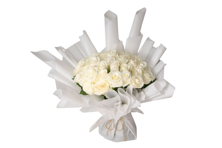 A bouquet of white roses with green leaves, wrapped in white paper and tied with a ribbon.